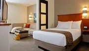 The image shows a neatly organized hotel room with a large bed and a separate sitting area, highlighting a comfortable and welcoming arrangement for guests.