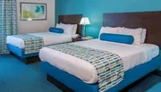 This image shows a brightly colored double bedroom with two beds, complementary bold blue and white decor, and a modern abstract painting adorning the wall.