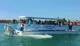 A group of people are enjoying a sunny day on a shelling and dolphin watch tour boat cruising through blue waters.