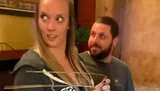 A woman holding divining rods looks to the side while a man standing behind her gazes at her.