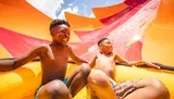 Two joyful children are sliding down a colorful water slide on a sunny day.