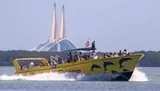 A yellow tour boat adorned with dolphin graphics speeds through the water with passengers on board, with a large cable-stayed bridge visible in the background.