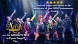 A group of lively performers are dancing on stage in colorful outfits with vibrant lighting effects in the background.