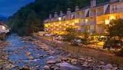 A multi-story hotel with lighted balconies overlooks a rocky riverbed in a twilight setting.