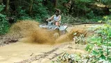 A person is riding an ATV through a muddy trail, splashing water and mud as they go.
