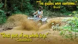 A person is riding an ATV through a muddy trail, splashing water and mud as they go.