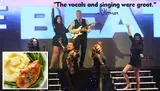 A group of performers is posing energetically on stage in front of a large sign, with a positive quote about their singing and an inset image of a meal featuring chicken, mashed potatoes, and green beans.