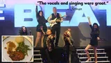 A group of performers is posing energetically on stage in front of a large sign, with a positive quote about their singing and an inset image of a meal featuring chicken, mashed potatoes, and green beans.
