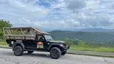 A modified off-road vehicle is parked on a scenic overlook with expansive views of rolling hills and cloudy skies.