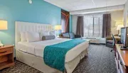 The image depicts a neatly arranged hotel room with a large bed, vibrant accent wall, and contemporary furnishings.