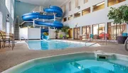 The image shows an indoor swimming pool area with a waterslide and a hot tub within a hotel or leisure complex.