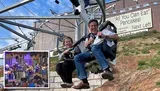 Two people are smiling and enjoying a ride on an alpine coaster near a sign advertising All You Can Eat Pancakes!