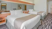 The image shows a tidy hotel room with two neatly made queen-size beds, a large mirror, and modern furnishings.