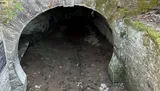 The image shows a dark, arched stone tunnel entrance, partially covered in moss.
