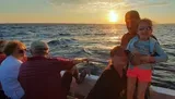 A group of people enjoys a scenic sunset aboard a boat, with a child in sunglasses smiling at the forefront.