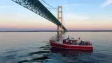 A tour boat named Ugly Anne is cruising near a large suspension bridge during a calm evening.