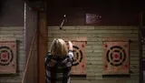 A person is seen throwing an axe towards a target in an indoor axe-throwing venue.