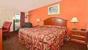 The image shows a hotel room with a brightly patterned bedspread, warm orange walls, and basic furnishings including a work desk, chair, and nightstands.