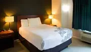 The image shows a neatly arranged hotel room with a queen-sized bed, two bedside lamps, and a patterned bed runner at the foot of the bed.
