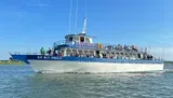 The image shows a large boat named New Inlet Princess from the Crazy Sister Marina, filled with passengers, cruising on the water with a promise of guaranteed dolphin sightings advertised in bold lettering above.