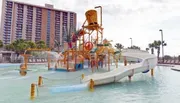 A colorful water playground with slides and splash features in front of a hotel complex.