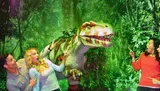 Three people appear to be playfully interacting with a Tyrannosaurus rex in a staged jungle setting.