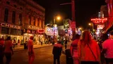 The image captures a vibrant night scene on a busy street lined with neon signs and people walking, suggesting a lively urban nightlife atmosphere.