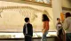 Several people, including young visitors, are observing the skeletal remains of a prehistoric creature on display in a museum exhibit.
