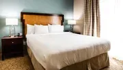The image shows a neatly made bed with white linens in a well-lit hotel room with matching nightstands and lamps on either side.