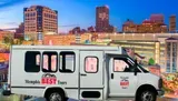 A tour van with Memphis BEST Tours on its side is parked with a backdrop of the Memphis skyline at twilight.