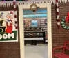 A person dressed as Mrs Claus looks surprised in a Christmas-themed kitchen while surrounded by individuals dressed as elves who are focused on preparing holiday treats