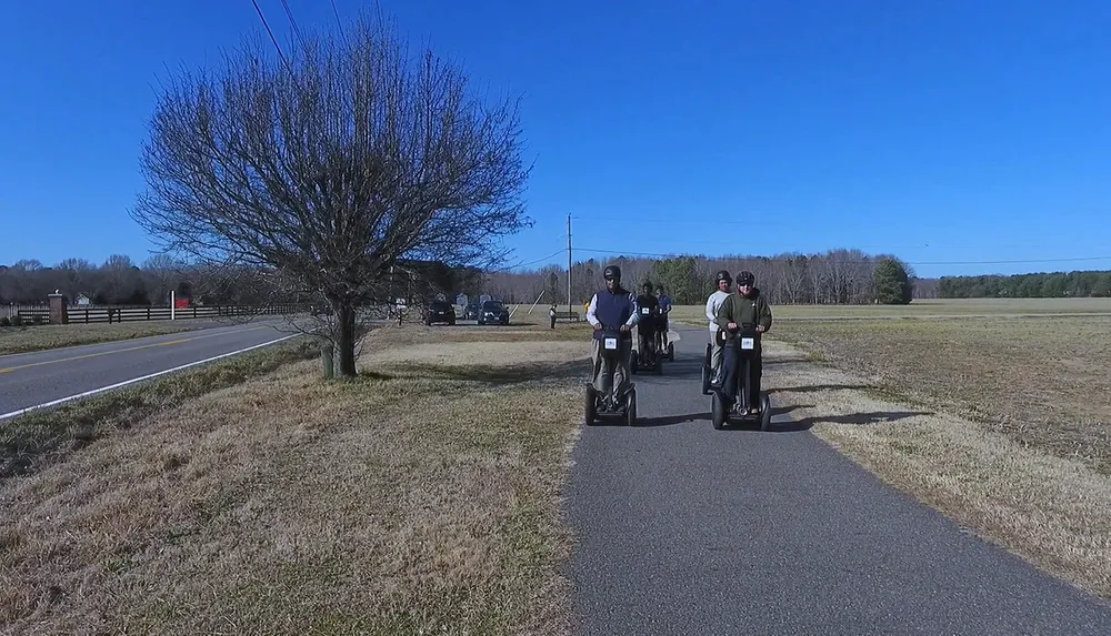 A group of people is riding Segways on a paved path in a scenic area with trees and a clear blue sky