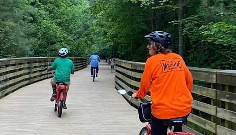 A group of individuals are cycling and walking on a wooden boardwalk surrounded by lush greenery