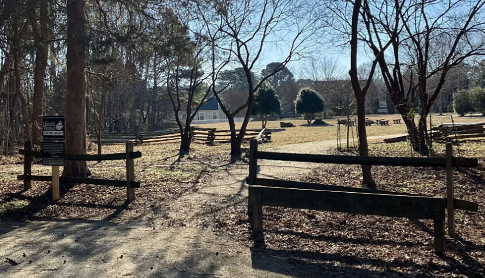 The image shows a peaceful rural park with bare trees split rail fences and a clear blue sky suggesting it may be a historic site during the autumn or winter months