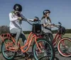 Two individuals wearing helmets are riding colorful bicycles across a grassy field