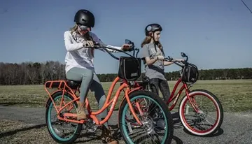 Two individuals wearing helmets are riding colorful bicycles across a grassy field.