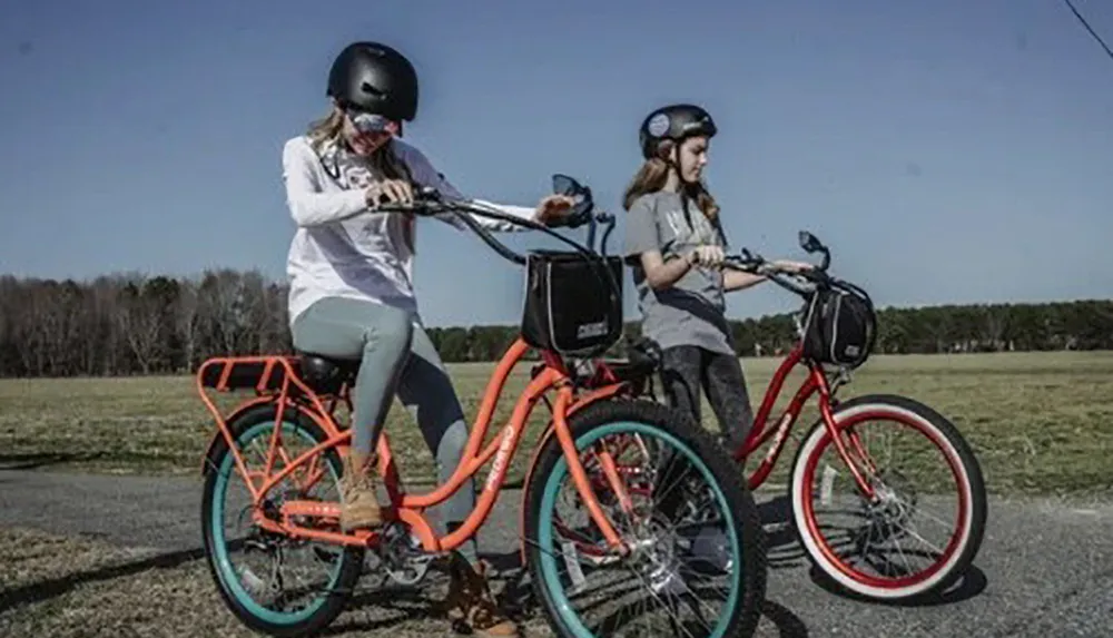 Two individuals wearing helmets are riding colorful bicycles across a grassy field