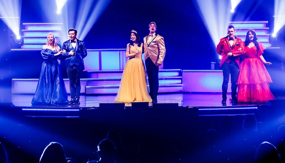 Six performers in formal attire sing under bright stage lights with women in elegant gowns and men in suits