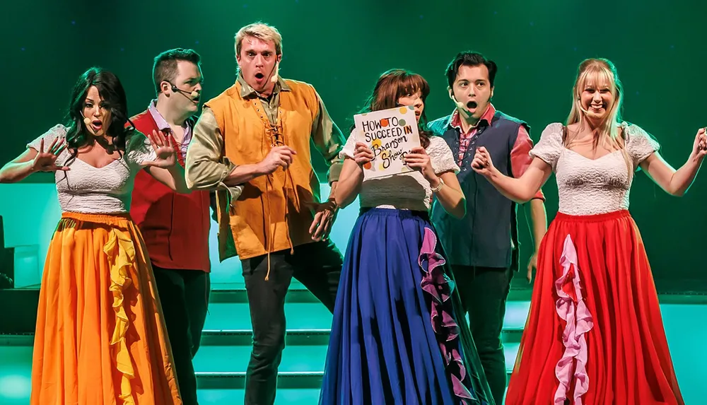 A group of performers on stage dressed in colorful costumes are energetically engaged in a lively act with one holding a sign that reads How to Succeed in Branson Shows