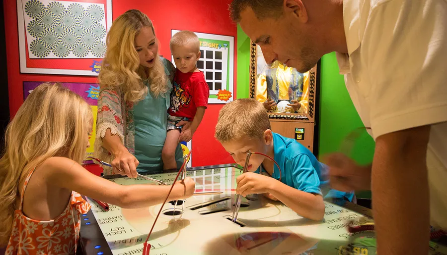 A family is engaged in an interactive exhibit, with adults and children focused on an activity at a table.