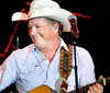 The image depicts a black and white portrait of a man wearing a cowboy hat and a patterned shirt gazing directly at the camera against a black background