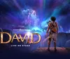 The image is a promotional poster for a stage production titled David showcasing a character gazing up at a cosmic event forming an angelic figure in a star-filled sky