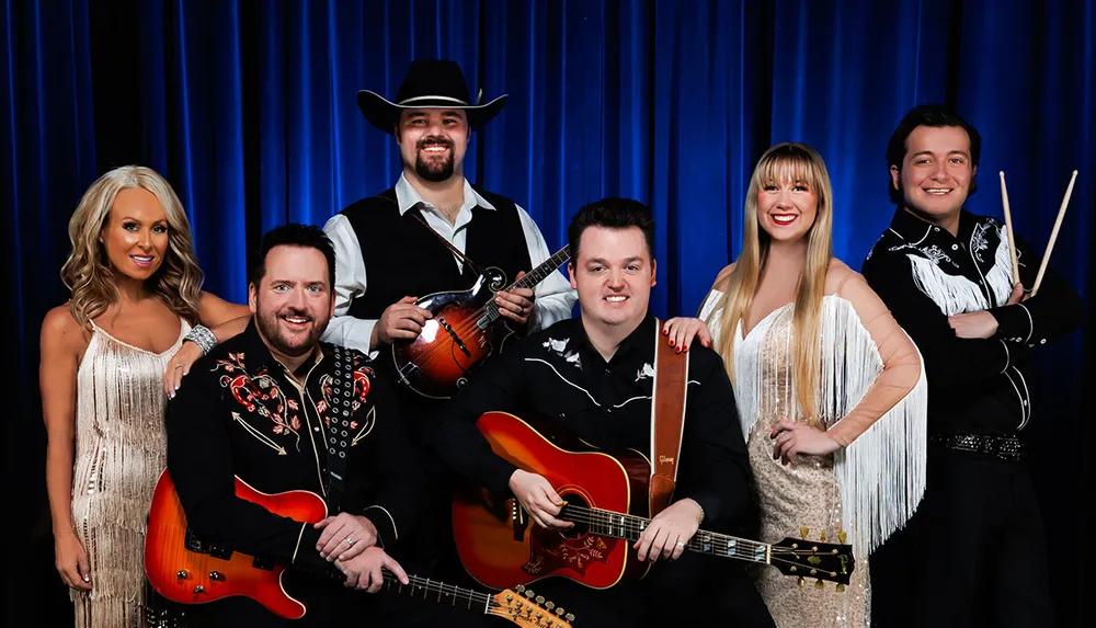 A group of musicians dressed in western attire posing with instruments against a blue curtain backdrop