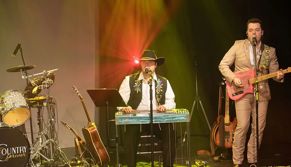 A country band performs on stage under colorful lighting featuring a musician in a cowboy hat playing a steel guitar and another in a tan suit playing an electric guitar