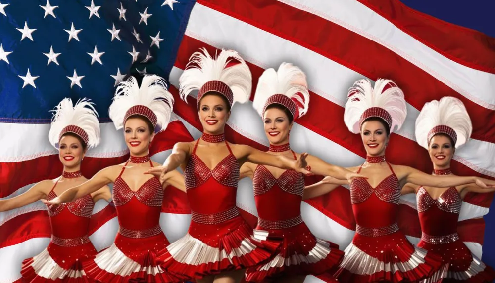 A group of dancers in red costumes pose in front of the American flag wearing white feathery headpieces