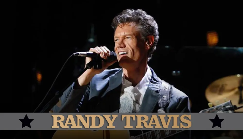 A person is singing into a microphone while playing a guitar with the name Randy Travis displayed at the bottom