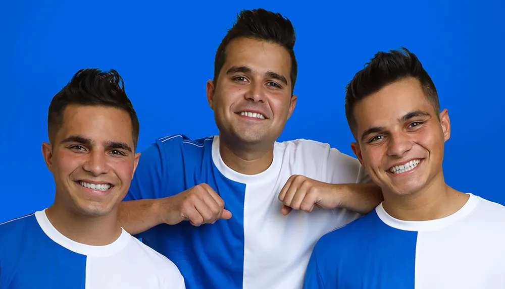 Three people wearing blue and white shirts are smiling against a blue background