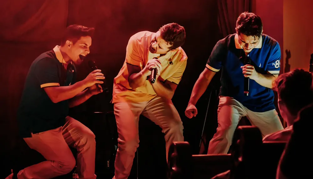 Three men are energetically singing into microphones on stage