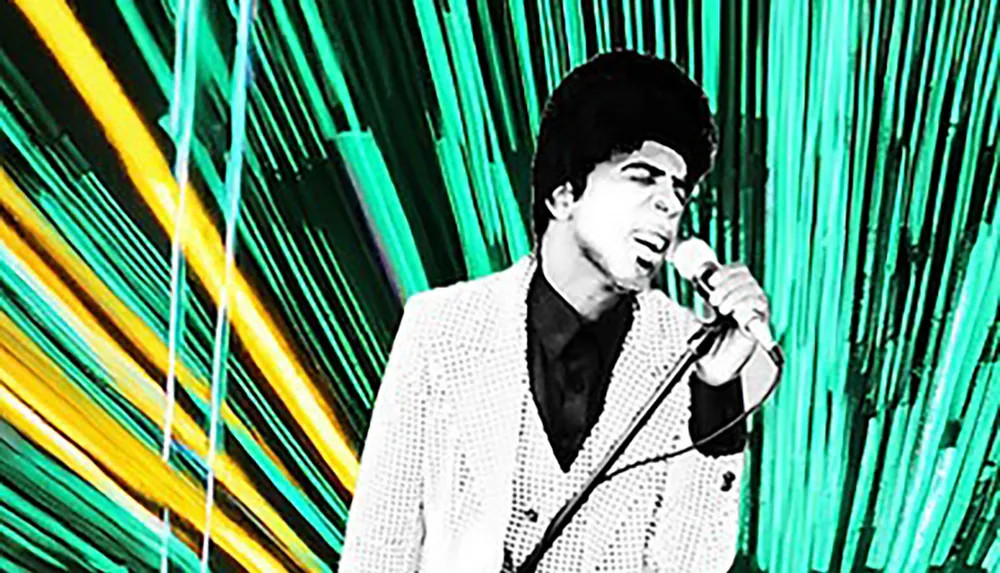 A person in a checkered suit passionately sings into a microphone against a vibrant green and yellow abstract backdrop