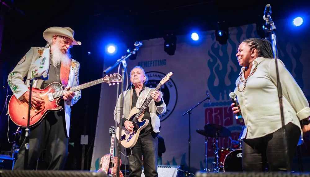 Three musicians are performing on stage with guitars and a microphone under bright stage lights